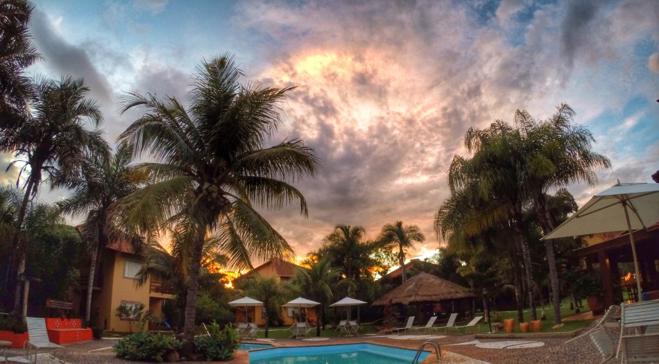 Área de lazer com piscina externa em hotel de Bonito MS ao pôr do sol, cercada por coqueiros e espreguiçadeiras.