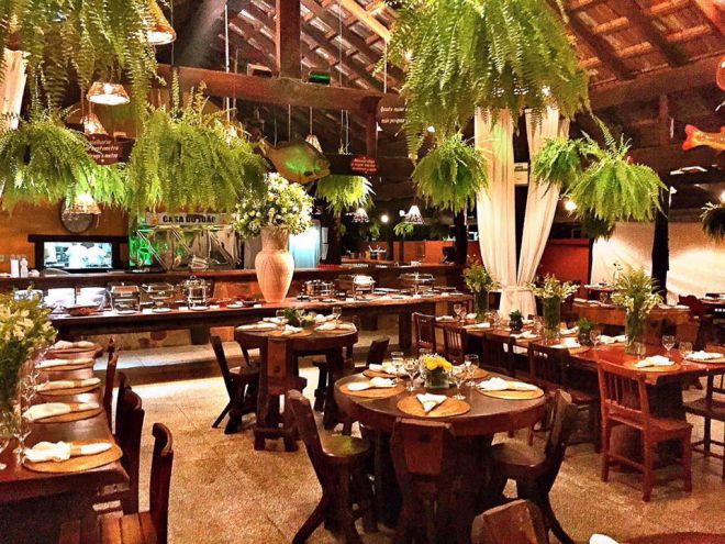 Interior de restaurante Casa do João em Bonito MS com decoração rústica, buffet self-service e muitas samambaias penduradas no teto.