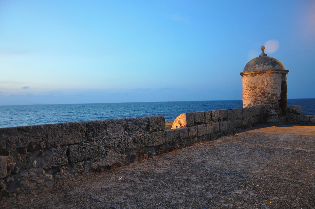 Pôr do sol visto das históricas Muralhas de Cartagena, destacando uma guarita de pedra antiga frente ao mar do Caribe.