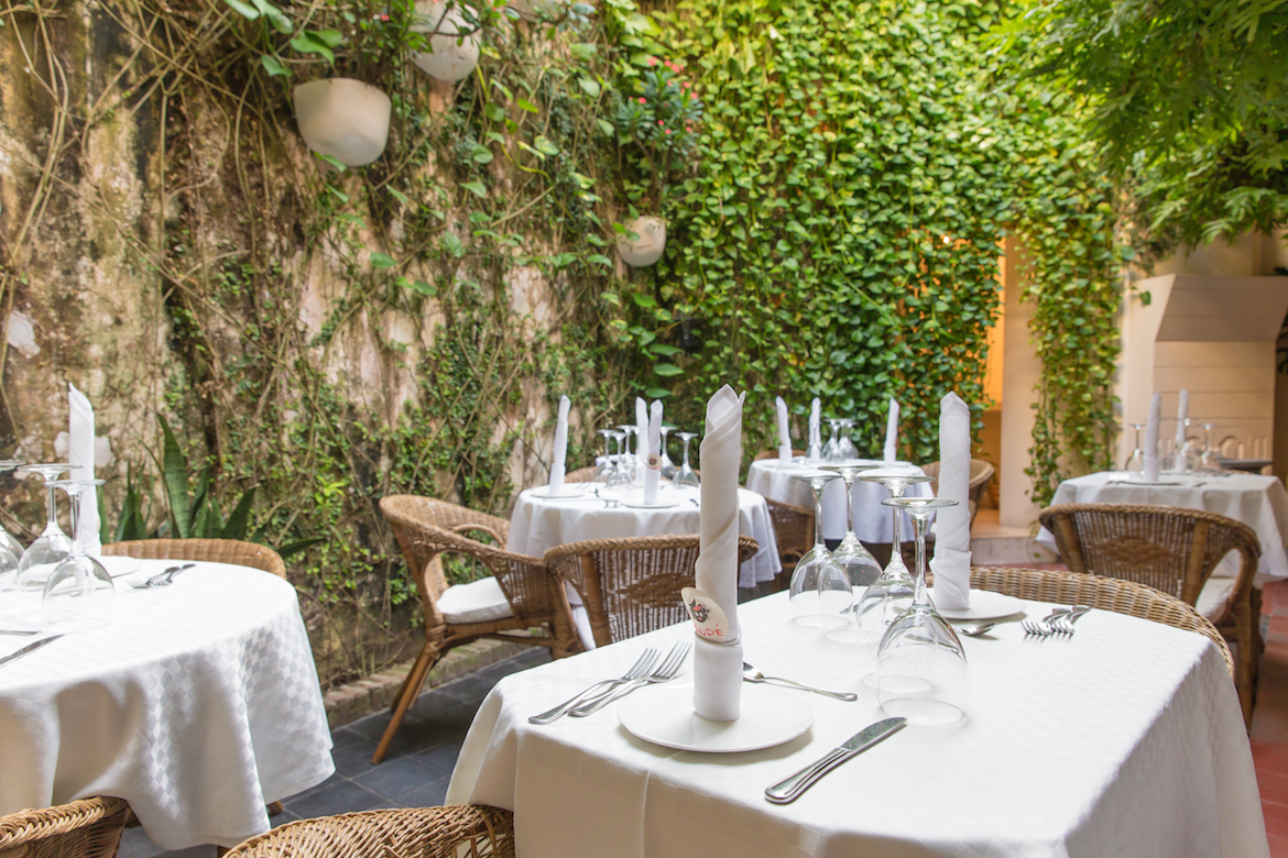 Interior sofisticado do Restaurante Candé em Cartagena, com mesas postas em um pátio cercado por plantas e paredes de pedra.