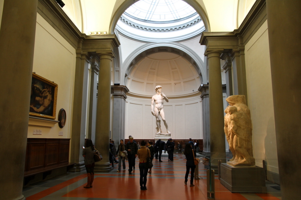 Turistas admirando a estátua original de Davi de Michelangelo, exposta sob a cúpula de vidro na Galleria dell'Accademia em Florença.
