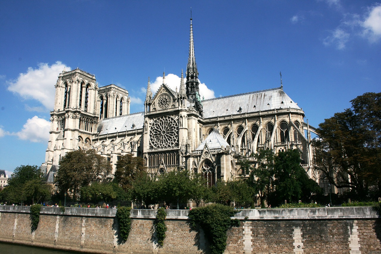 Vista exterior da Catedral de Notre Dame em Paris, exibindo a arquitetura gótica francesa, a rosácea e a torre sob um céu azul.