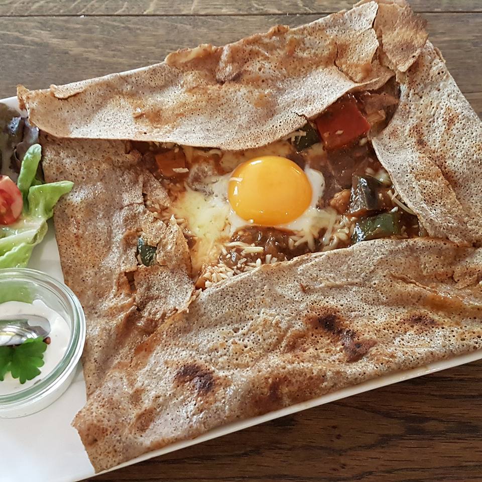 Uma Galette Bretonne (crepe de trigo sarraceno) tradicional, dobrada em quadrado com um ovo estalado no centro, servida com salada.