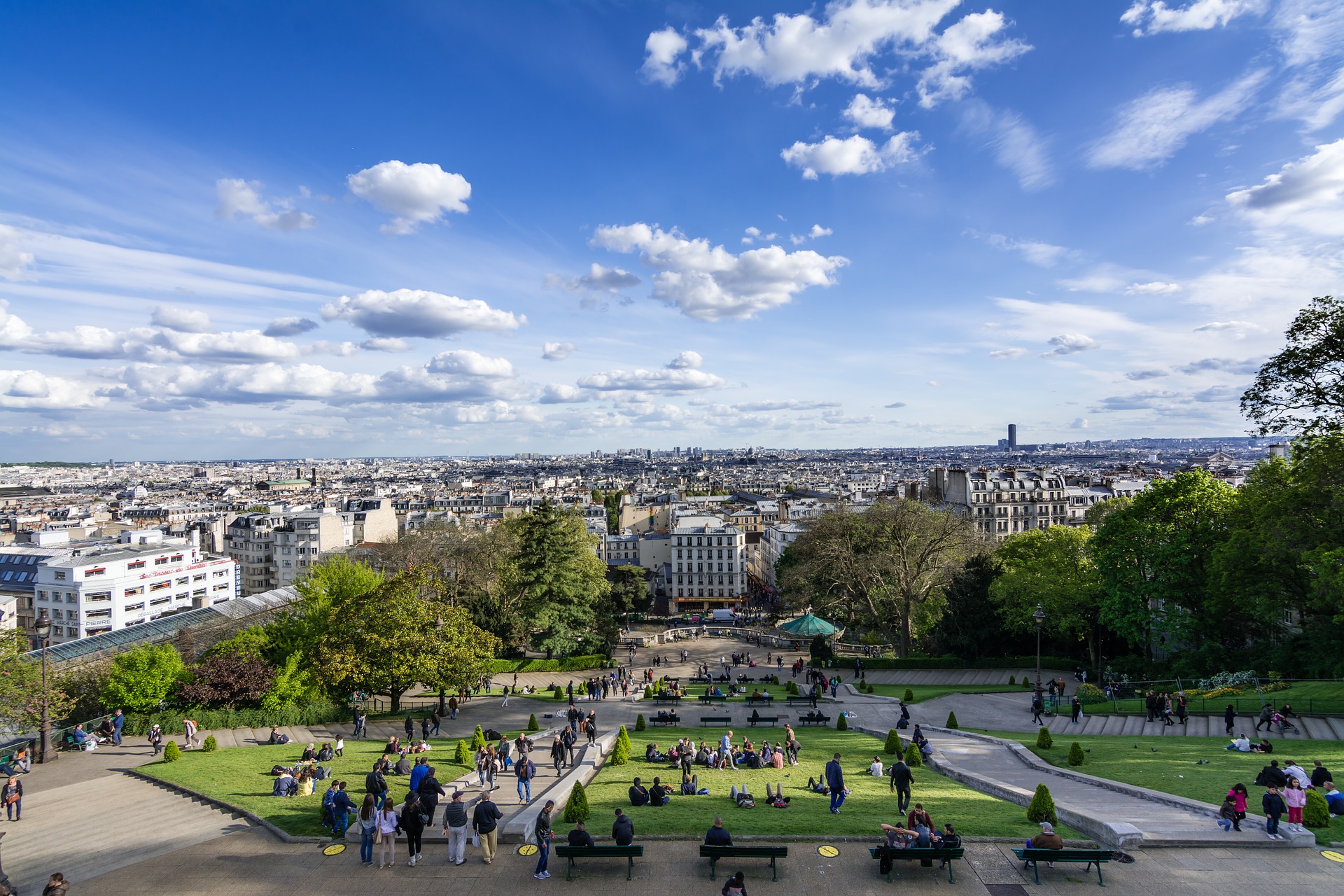 Turistas relaxando no gramado das escadarias da Basílica de Sacré-Cœur em Montmartre, com uma vista ampla da cidade de Paris ao fundo.