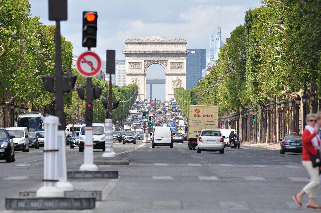 Vista da famosa Avenue des Champs-Élysées em Paris com tráfego intenso de carros, árvores alinhadas e o Arco do Triunfo ao fundo.