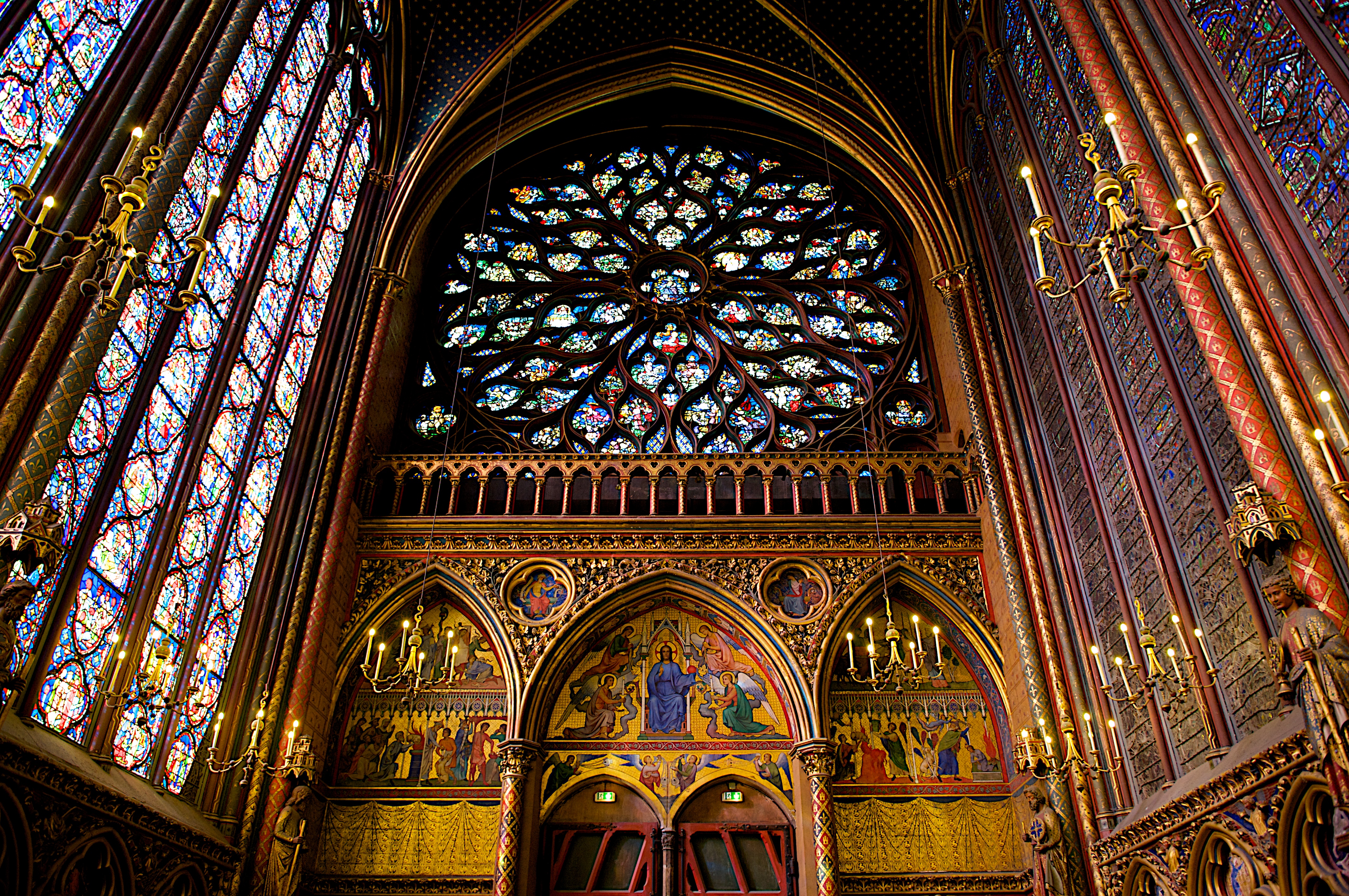 Interior da Sainte-Chapelle em Paris, destacando a arquitetura gótica impressionante, o teto abobadado e os imensos vitrais coloridos religiosos.