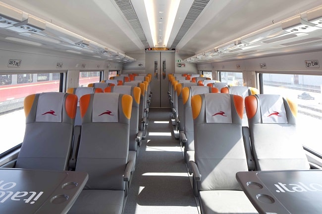 Interior moderno de um vagão do trem de alta velocidade Italo Treno, mostrando assentos cinza e laranja vazios.