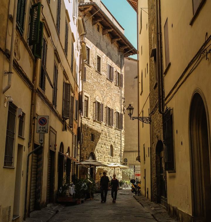 Vista da Via della Vigna Vecchia, uma rua estreita e charmosa no centro histórico de Florença, cercada por prédios antigos de arquitetura toscana sob a luz do sol.