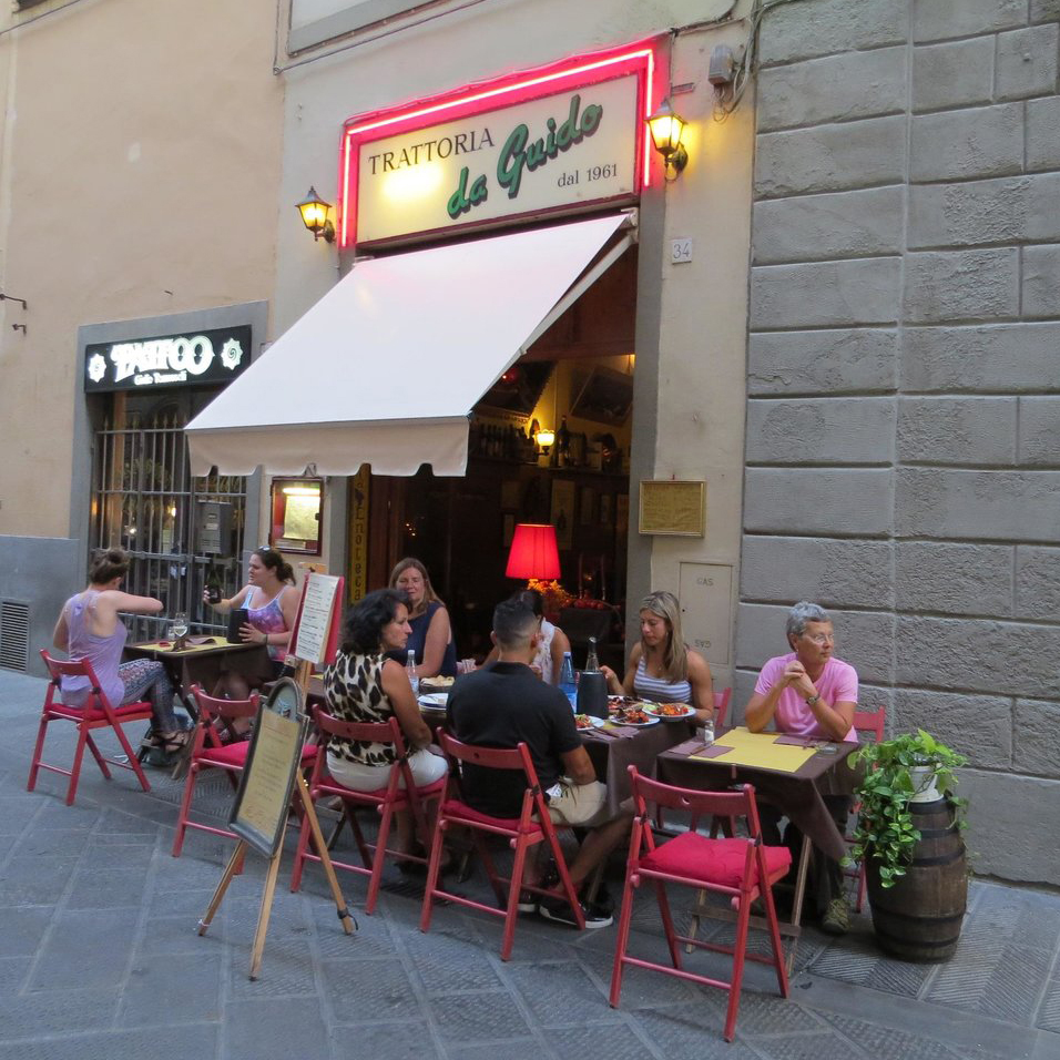 Clientes jantando nas mesas externas da Trattoria da Guido, um restaurante típico italiano nas ruas de Florença.