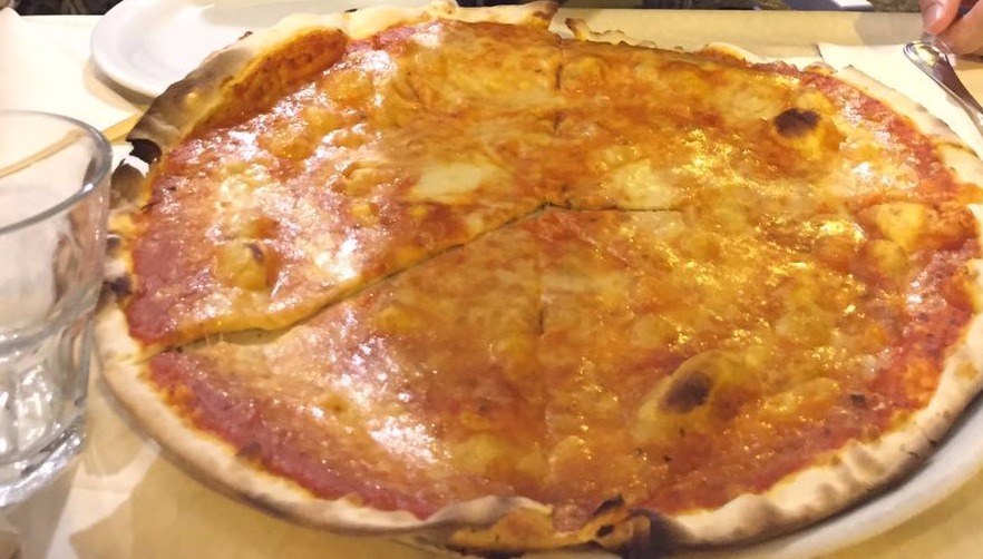 Pizza margherita inteira com borda crocante servida em um prato branco, gastronomia típica da Itália.